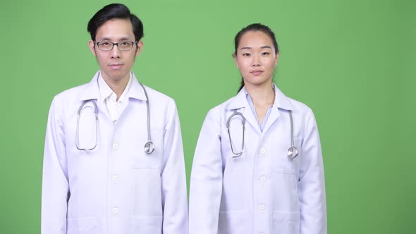 Young Asian Couple Doctors Pointing at Camera Together