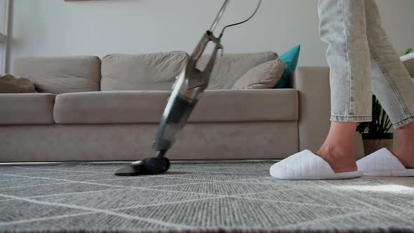Young Woman Legs in Sneakers Cleaning Carpet with Vertical Vacuum Cleaner While Cleaning the House