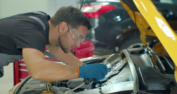 Mechanic Man with Lamp Working at Workshop. Car Repair Service. Professional Mechanic Is Working alt
