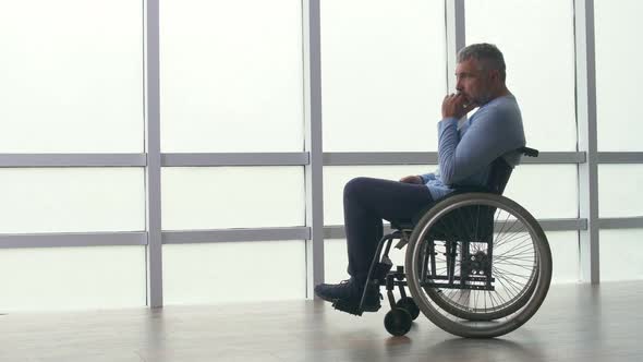 Sad Lonely Middleaged Man Sitting in a Wheelchair By the Window alt