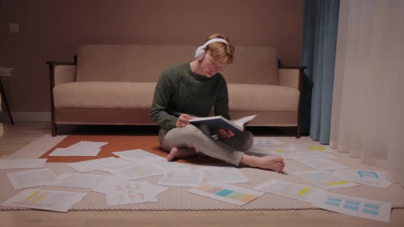 Guy Sits on the Floor Surrounded By Papers and Notes Listens Music at Home alt