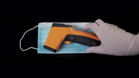 Doctor Puts a Contactless Infrared Thermometer on a Medical Mask. The Doctor Holds a Thermometer in alt