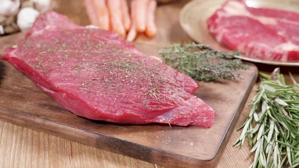 Fresh, Raw Steak, Well Seasoned on a Wooden Board with Thyme and Rosemary alt