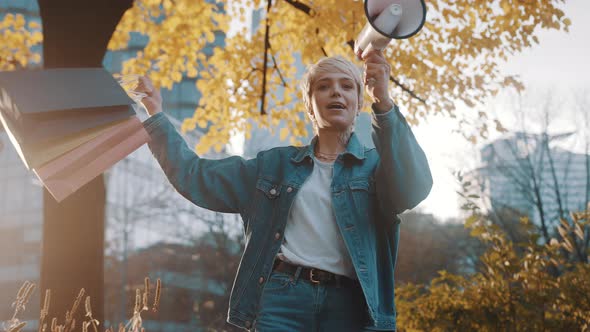 November Sales. Young Woman with Shopping Bags Announcing Sales Season with Megaphone in the City alt