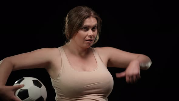 Confident Attractive Plus Size Woman Posing with Soccer Ball at Black Background Gesturing Thumb Up alt