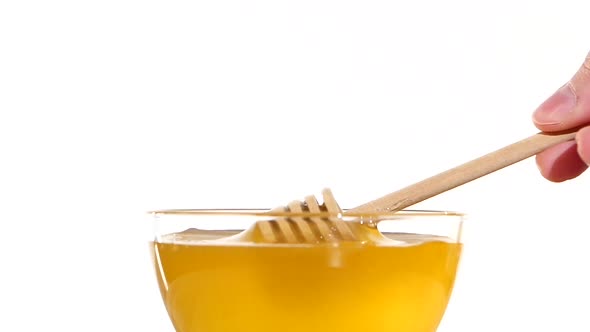Hand Taking Honey From Bowl Using Wooden Spoon Dipper, Pit It Up, on White, Slow Motion alt