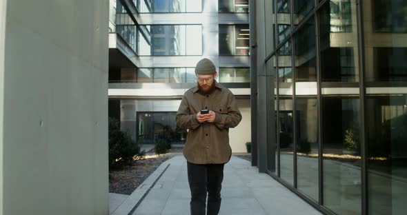 A Young Man is Typing on a Mobile Phone While Walking Around the Business Center alt