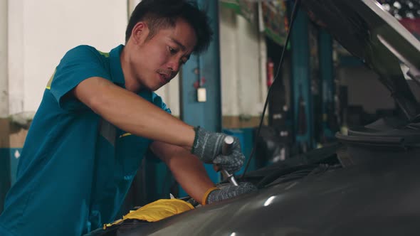 Skillful Asian guy in uniform fixing car at mechanics garage at night. alt
