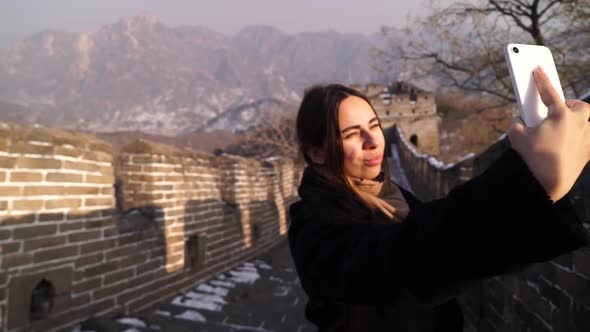Beautiful Woman Travelling Asia, Stands on the Great Wall of China Taking Selfies at Sunset in