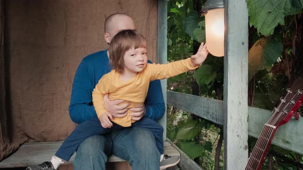 Dad and a Cute Little Child are Sitting on the Porch of a Country House