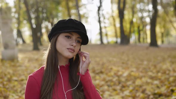 Happy Girl Relaxing in Autumn Park and Listening to the Music with Earphones alt