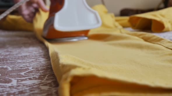 Woman Ironing Yellow Trousers with an Orange Iron Closeup DOF
