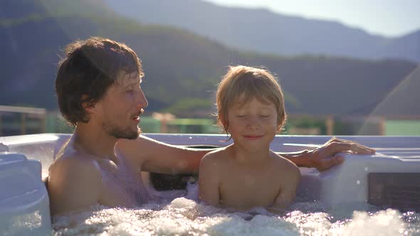A Young Man and His Son Relaxing in the Hot Tub on a Rooftop with a View on Mountains alt