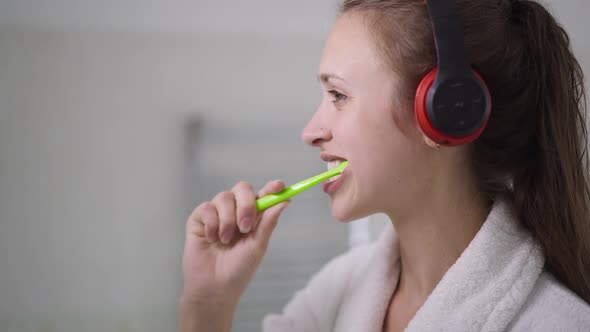 Side View Face of Concentrated Slim Beautiful Young Woman in Headphones Brushing Teeth in Slow alt
