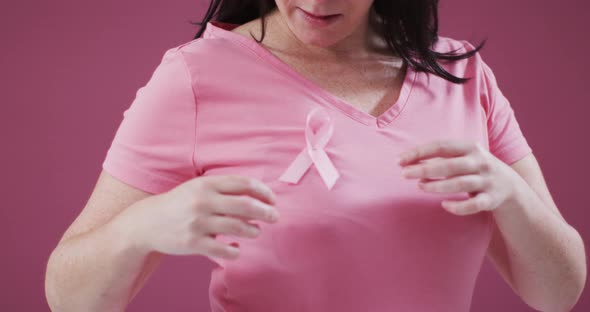 Mid section of a woman touching the pink ribbon on her chest against pink background alt