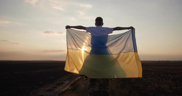 A Ukrainian Soldier Carries a Child in His Arms Holding the Flag of Ukraine alt