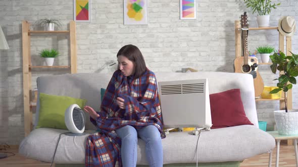 Frozen Young Woman in the Living Room and Basking Next To Electric Heaters alt