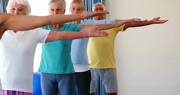 Trainer assisting senior citizens in practicing yoga alt