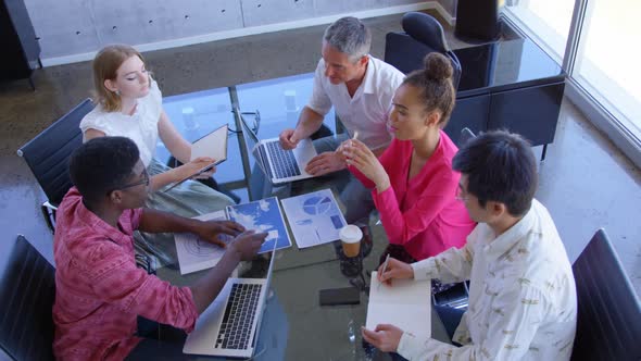 Multi-ethnic business colleagues discussing over graphs in a meeting at modern office 4k alt