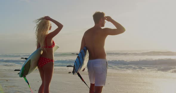 Couple standing with surfboard on the beach 4k