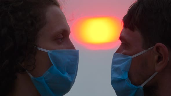 Loving couple in protective masks watching sunset. Couple looks into each other eyes