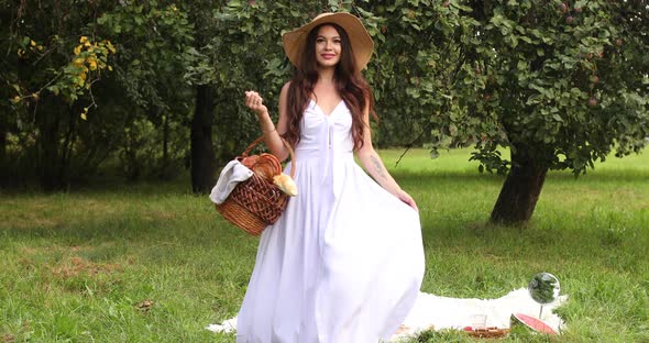 Young Beautiful Woman Walks Through the Garden with a Basket in Her Hands and Smiles