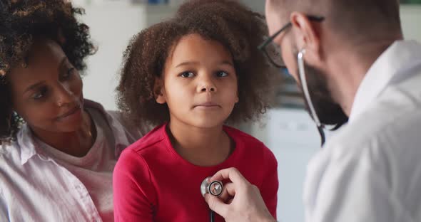 Doctor Examining Little African Girl By Stethoscope in Clinic Office alt