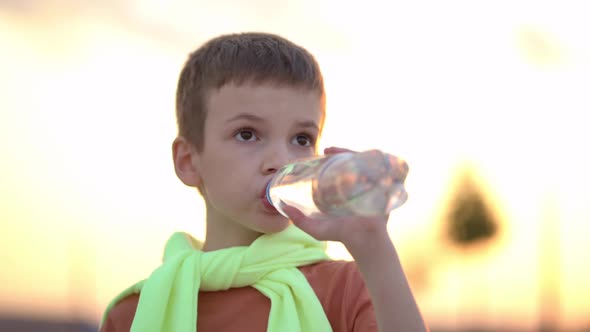 Young Man Drinking Water From a Plastic Bottle in the City at Sunset