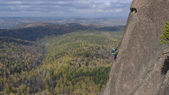 Aerial View of a Man Climbing a Rope To the Top of a Mountain Overlooking the Autumn Forest
