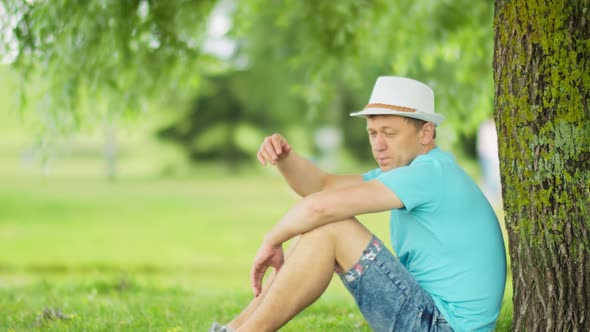 Lonely Man Resting in the Shade of a Tree While Sitting in the Park Side View alt