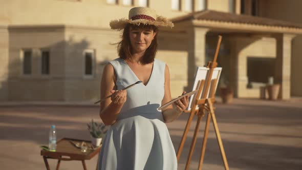 Medium Shot Portrait of Charming Smiling Talented Woman Holding Paint Palette and Brush Looking at alt