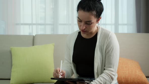 Woman Sits on the Sofa at Home Drawswrites and Uses a Pen with a Digital Tablet Computer alt