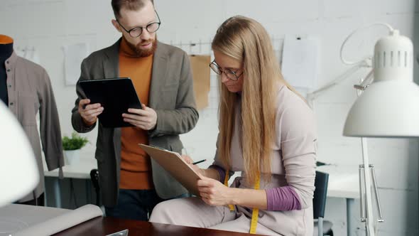 Young Female Fashion Designer Talking to Male Colleague Using Tablet Working in Studio Together alt