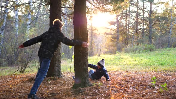 A Teenager Plays with a Child Runs in the Park Around a Tree and Catches Up with Him alt