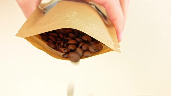 Coffee beans pouring from kraft paper pouch bag on light background cafe 4K Freshly roasted grains