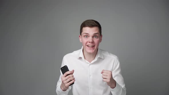 A Young Emotional Guy Screams with Joy Showing His Phone