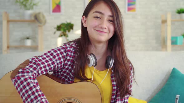 Beautiful Asian Girl with a Guitar in the Living Room of the Houselooking at the Camera Smiling alt