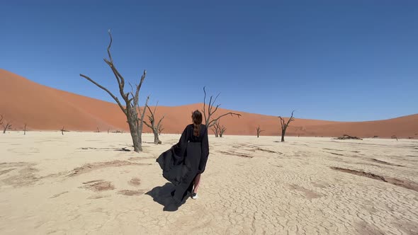 A Young Woman in a Long Black Dress Walks Through the Desert