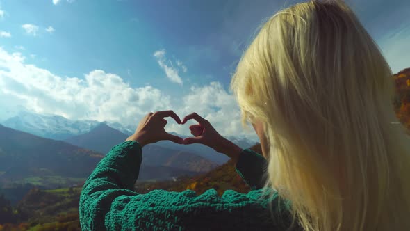 Woman on hike on top of mountain makes heart shaped finger frame with her hands. alt