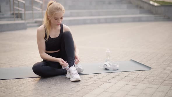 Fitness Young Woman Sitting Yoga Mat Outdoors Tie Shoelaces on White Sneakers Dressed Black alt