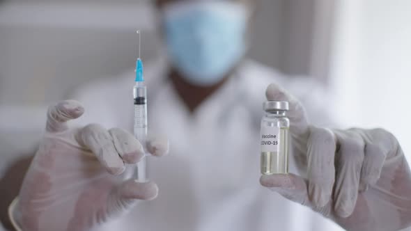Closeup Syringe and Ampoule with Coronavirus Vax in Male African American Hands in Gloves alt