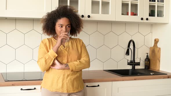 Attractive African Woman is Drinking Water From Glass Standing in the Kitchen alt
