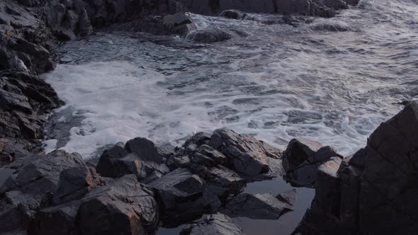 Calm ocean waves rolling into rocky coast line at sunset. Tripod slow motion shot in 4K. alt