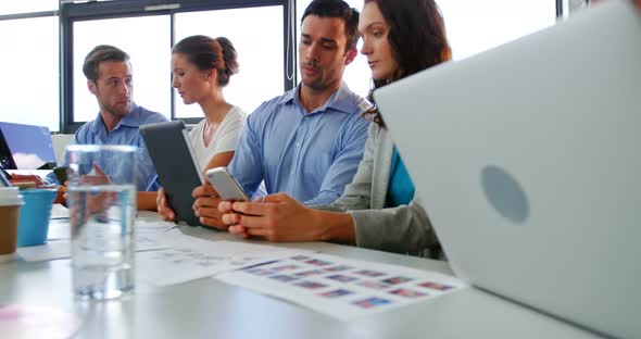 Business executives discussing over laptop, digital tablet and mobile phone alt