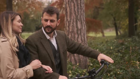 Handsome young couple in the autumn park with electrical bicycle