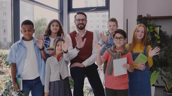 Male Teacher with Middle School Children Looking at Camera and Waving Hands alt