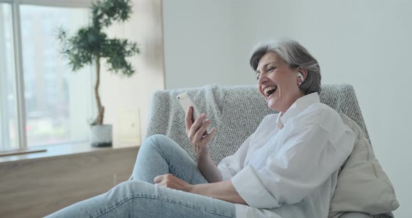 Happy Senior Old Woman in Headphones Looking Mobile Screen Enjoying Video Meeting alt