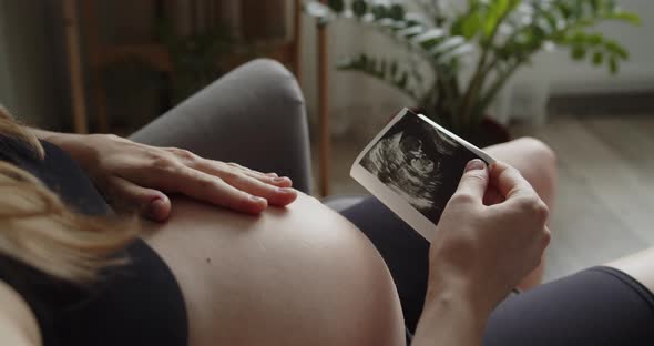 A Young Pregnant Woman Holds and Looks at Ultrasound Picture of Her Baby alt