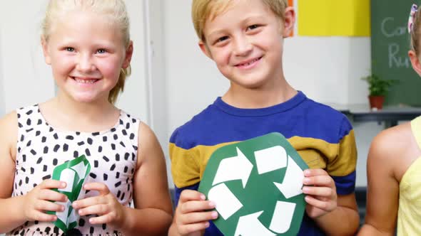 School kids holding recycling symbols and globe in classroom alt