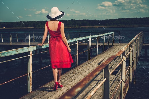 Stylish woman in white hat and red dress standing on old wooden pier - Stock Photo - Images